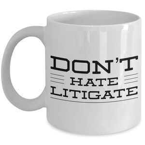 May include: White ceramic coffee mug with black text that reads "DON'T HATE LITIGATE".