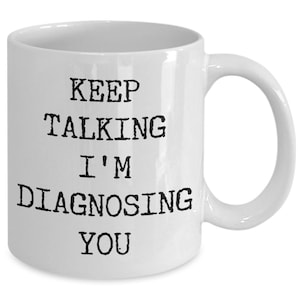 May include: White ceramic coffee mug with black text that reads "Keep Talking I'm Diagnosing You".