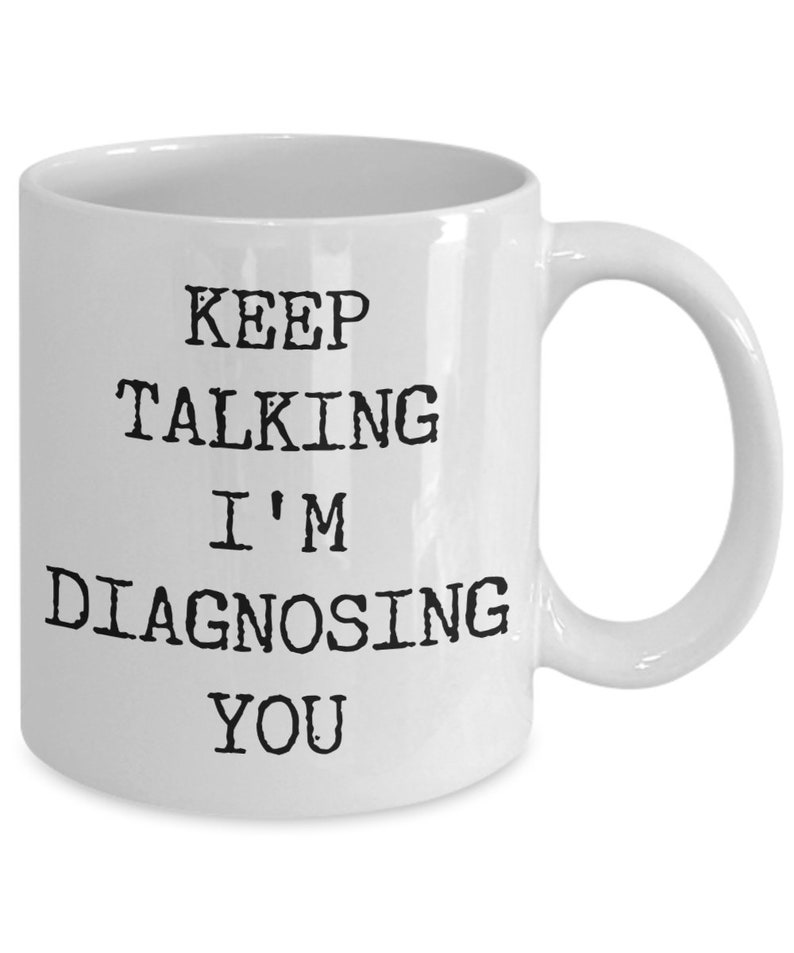 May include: White ceramic coffee mug with black text that reads "Keep Talking I'm Diagnosing You".