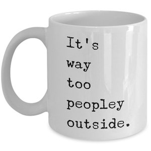 May include: White ceramic coffee mug with black text that reads "It's way too peopley outside."