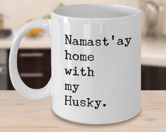 May include: White ceramic coffee mug with black text that reads "Namaste'ay home with my Husky."