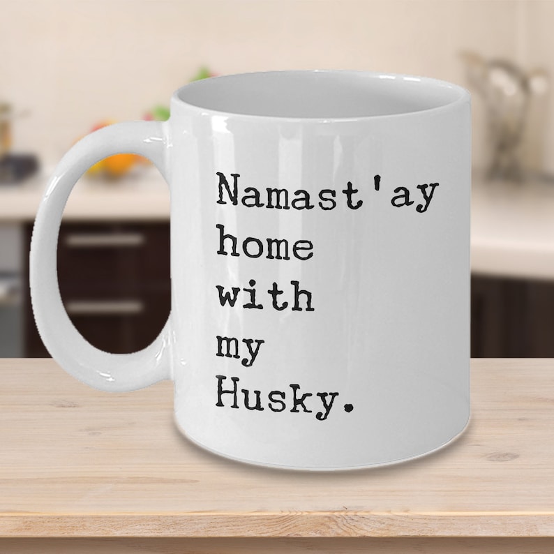 May include: White ceramic coffee mug with black text that reads "Namaste'ay home with my Husky."