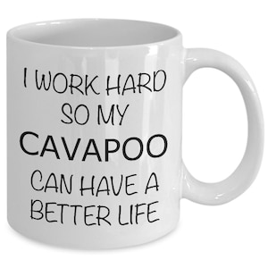 May include: White ceramic coffee mug with black text that reads "I work hard so my Cavapoo can have a better life."