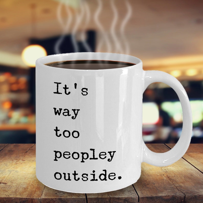 May include: White ceramic coffee mug with black text that reads "It's way too peopley outside."