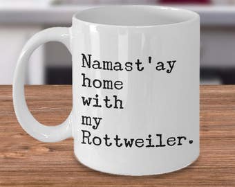 May include: White ceramic coffee mug with a black inscription that reads "Namaste'ay home with my Rottweiler."