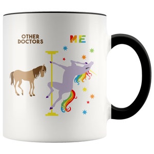 May include: White ceramic coffee mug with a black rim and handle. The mug features a graphic of a unicorn with a rainbow tail, dancing on a pole. The text "Other Doctors" is on the left side of the mug and "ME" is on the right side.