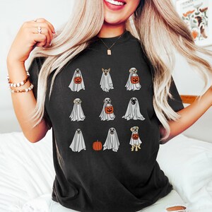 Peut inclure: Un t-shirt noir avec un motif de chiens habill&eacute;s en fant&ocirc;mes pour Halloween. Les chiens tiennent des citrouilles et portent des costumes de fant&ocirc;mes.