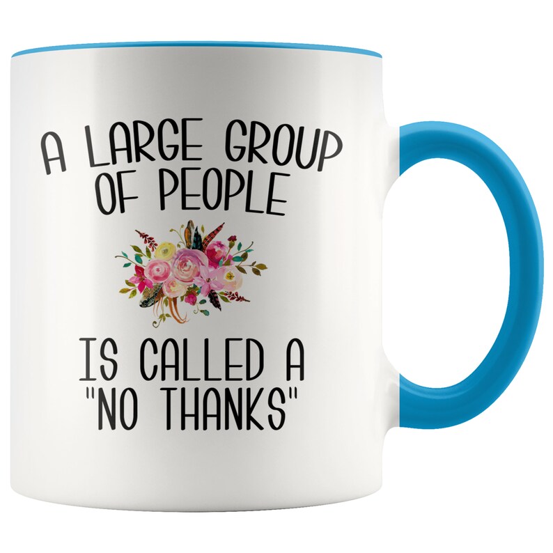 May include: White ceramic coffee mug with a blue rim and handle. The mug features a floral design and the text "A large group of people is called a "no thanks""