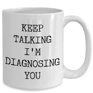 May include: White ceramic coffee mug with black text that reads "Keep Talking I'm Diagnosing You".