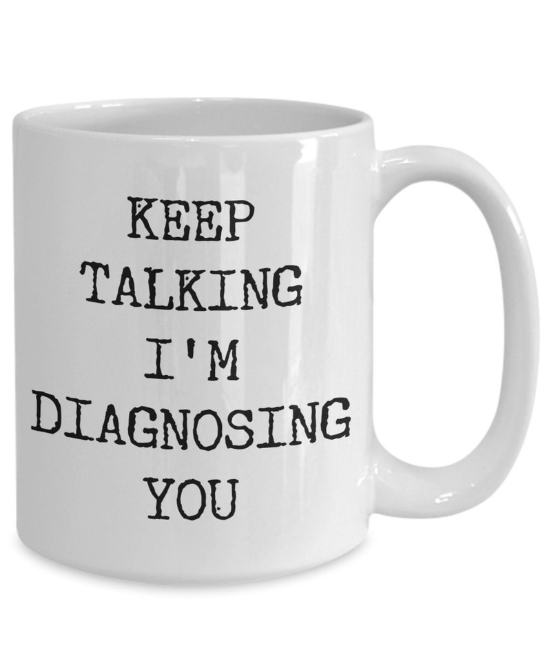 May include: White ceramic coffee mug with black text that reads "Keep Talking I'm Diagnosing You".