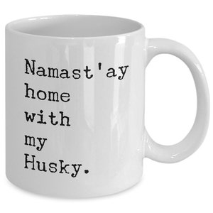 May include: White ceramic coffee mug with black text that reads "Namaste'ay home with my Husky."