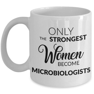 May include: White ceramic mug with a curved handle. The mug features black text that reads "ONLY THE STRONGEST Women BECOME MICROBIOLOGISTS". The mug is designed for microbiologists.