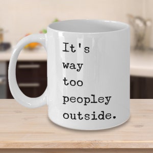 May include: White ceramic coffee mug with black text that reads "It's way too peopley outside."