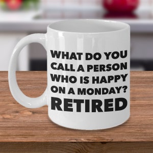 Könnte beinhalten: Eine weiße Keramik-Kaffeetasse mit schwarzem Text, der lautet: "Was nennt man eine Person, die an einem Montag glücklich ist? Rentner."