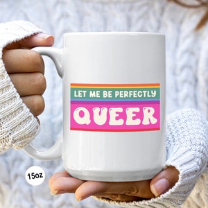 May include: White ceramic mug with a rainbow stripe design and the text "Let me be perfectly QUEER" in pink letters.