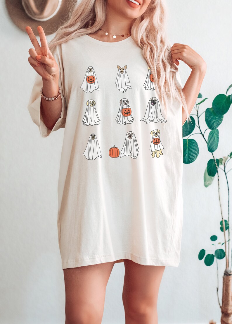 Peut inclure: Un t-shirt blanc avec un motif de chiens habill&eacute;s en fant&ocirc;mes pour Halloween. Les chiens tiennent des citrouilles et portent des draps de fant&ocirc;mes.