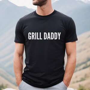 May include: A black t-shirt with the text "GRILL DADDY" printed in white on the front.