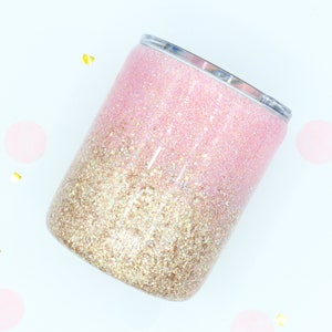 May include: A pink and gold glitter tumbler with a gradient design. The tumbler is made of stainless steel and has a lid.