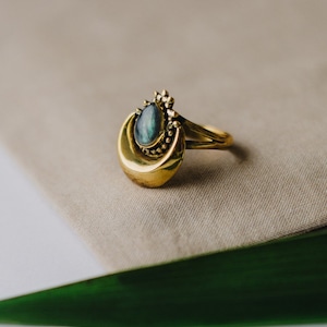 Op de afbeelding: Een gouden ring met een halve maan ontwerp en een donkergroene edelsteen in het midden.