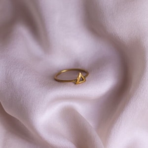 May include: A gold triangle ring on a white fabric background.