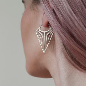 May include: A silver geometric hoop earring with a triangular shape and a sunburst design.