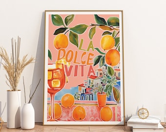 May include: A framed art print with the words "LA DOLCE VITA" in orange and yellow lettering. The artwork features oranges, green leaves, and a view of a coastal town. A cocktail glass is in the foreground.