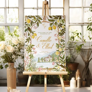 May include: A wedding welcome sign with a floral design featuring lemons, flowers, and a picturesque Italian villa. The sign reads "Welcome to the wedding of Camille & Elliot, Saturday, May 21, 2023."