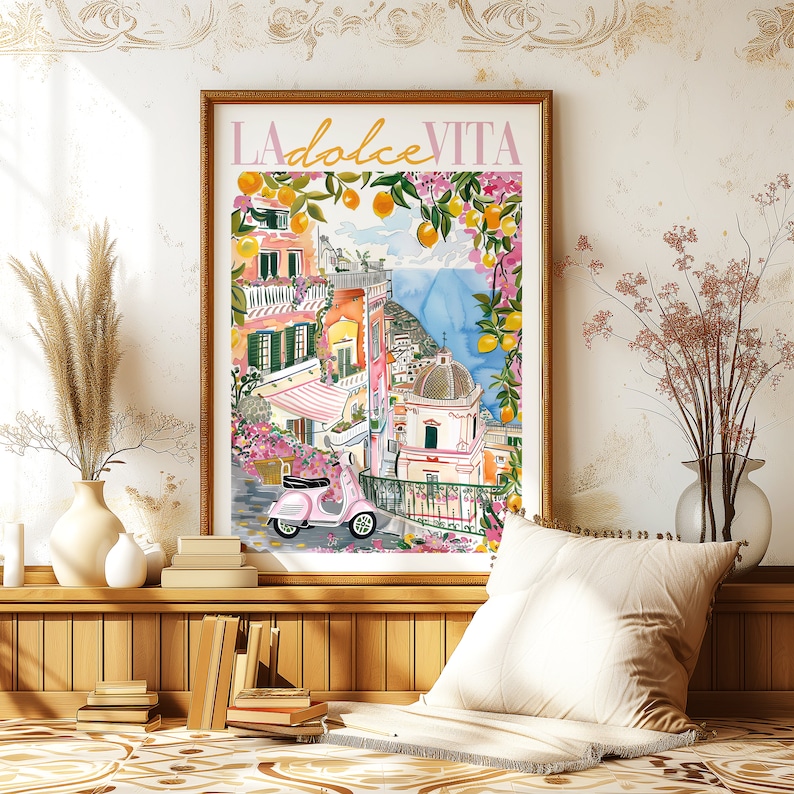 以下が含まれることがあります： 水彩画で描かれた、カラフルなイタリアの村の風景。手前にピンクのスクーターが描かれている。絵は額縁に入っていて、白い壁に飾られている。絵の上部にはピンクの文字で「LA dolce VITA」と書かれている。