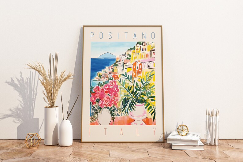 Może przedstawiać: Kolorowy plakat z akwarelową ilustracją Positano we Włoszech. Plakat przedstawia widok kolorowych budynk&oacute;w miasta, błękitnego morza i zielonej rośliny w doniczce. Tekst "Positano, Włochy" jest wydrukowany na kremowym tle białym kolorem.