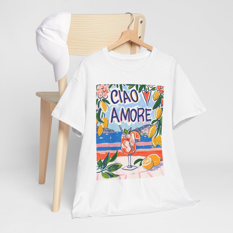 May include: White t-shirt with a colorful graphic print of a glass of orange juice, lemons, flowers, and the text "Ciao Amore" with a red heart.