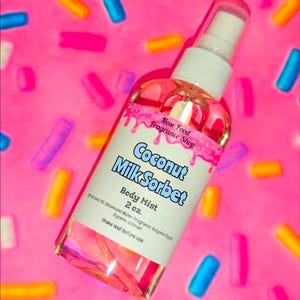 Puede incluir: Un frasco transparente de bruma corporal con una etiqueta blanca con el texto "Coconut Milk Sorbet" y "Nose Food Fragrance Shop". El frasco es de 59 ml y está sobre un fondo rosa con chispas de colores.