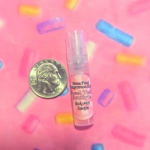 May include: A clear body mist sample bottle with a pink label that reads "Nose Food Fragrance Shop Sweet Tooth Boutique Body Mist Sample" next to a US quarter on a pink background with colorful sprinkles.