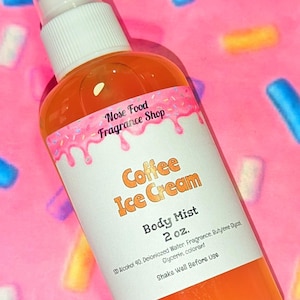 May include: A clear spray bottle with a white cap and a label that reads "Coffee Ice Cream Body Mist 2 oz." The bottle contains an orange liquid. The background is pink with colorful sprinkles.