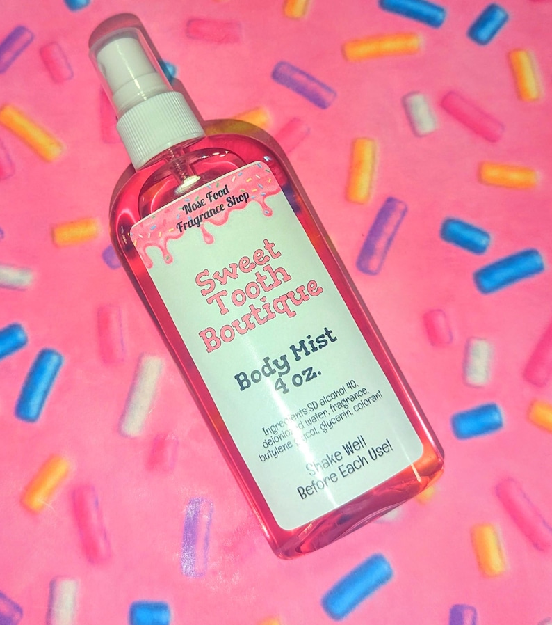May include: A pink body mist spray bottle with a white label that reads "Sweet Tooth Boutique Body Mist 4 oz." The bottle is filled with a pink liquid and has a white spray nozzle. The background is pink with colorful sprinkles.