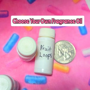Może przedstawiać: Biała butelka z napisem "Fruit Loops" i kremową zakrętką, obok monety. Tekst "Choose Your Own Fragrance Oil" jest wyświetlany na białym banerze. Tło jest różowe z niebieskimi i żółtymi kształtami.