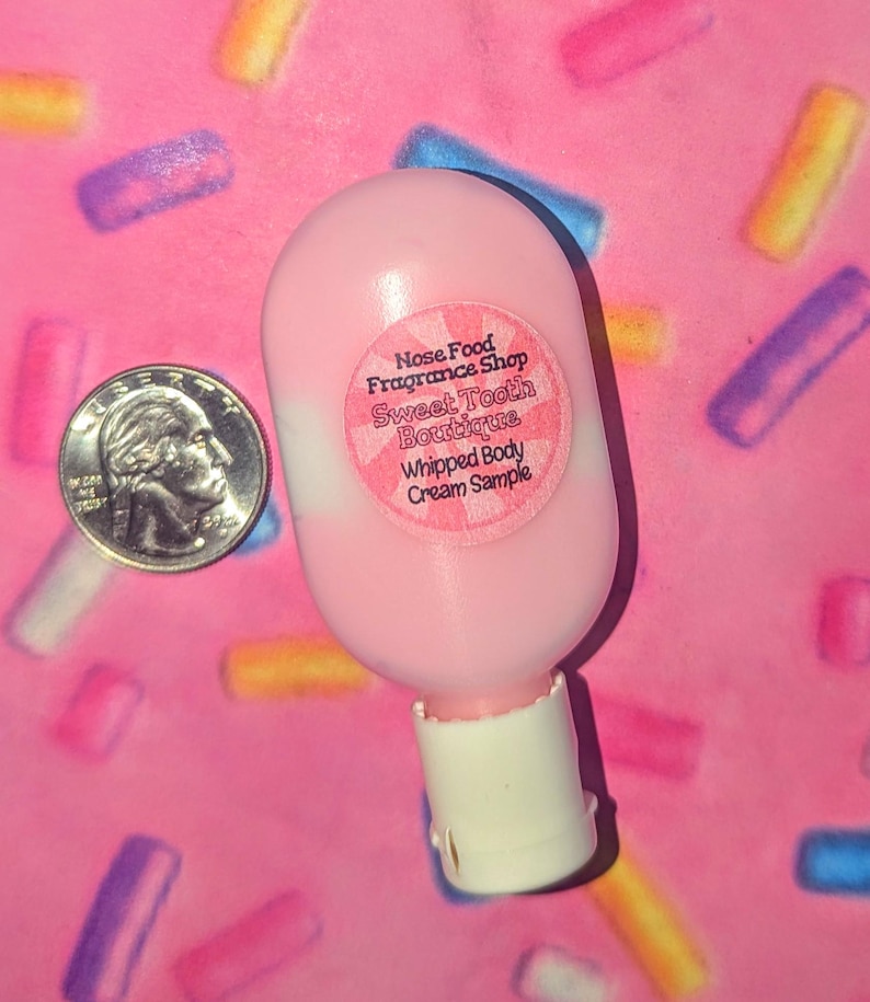 May include: A pink whipped body cream sample bottle with a white base and a round sticker that reads "Nose Food Fragrance Shop Sweet Tooth Boutique Whipped Body Cream Sample." A U.S. quarter is next to the bottle.
