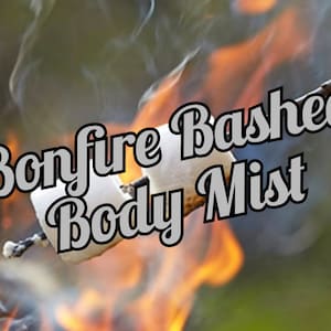 Puede incluir: Un malvavisco asándose sobre una hoguera, con llamas y humo de fondo. El texto "Bonfire Bashed Body Mist" está superpuesto en la imagen, sugiriendo un producto para el cuidado corporal.