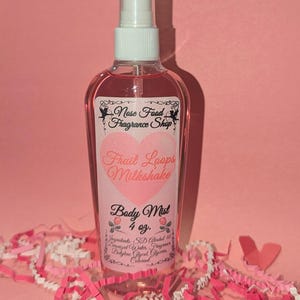 Puede incluir: Un frasco transparente de bruma corporal con un pulverizador blanco, lleno de líquido rosa. La etiqueta dice "Nose Food Fragrance Shop" y "Fruit Loops Milkshake Body Mist 4 oz." Decoraciones rosas y blancas en el fondo.