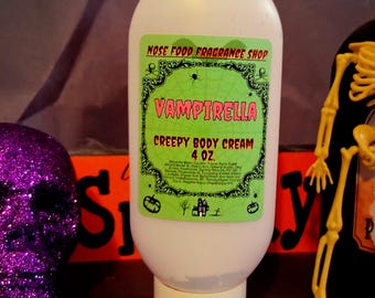 以下が含まれることがあります： 緑とピンクのラベルが付いた「Vampirella Creepy Body Cream」の白いボトル。ラベルにはクモの巣のデザインと「Nose Food Fragrance Shop」の文字が描かれています。 ボトルは118 mlです。