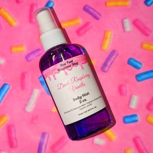 May include: A purple body mist bottle with a white spray nozzle. The label reads "Dark Raspberry Vanilla" and "Body Mist 2 oz." The background is pink with colorful sprinkles.