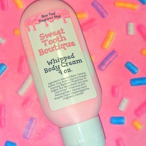 May include: A pink bottle of "Sweet Tooth Boutique" whipped body cream, 4 oz. The label features pink text and a pink and white design. The background is a pink surface with colorful sprinkles.