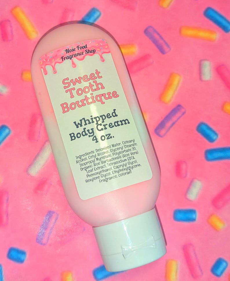 May include: A pink bottle of "Sweet Tooth Boutique" whipped body cream, 4 oz. The label features pink text and a pink and white design. The background is a pink surface with colorful sprinkles.