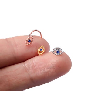 May include: Three nose rings with a blue evil eye design. The rings are made of silver, gold, and rose gold.