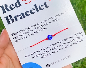 Pode incluir: Pulseira de fio vermelho com um amuleto azul de olho turco. A pulseira está amarrada em torno de uma mão e o cartão diz "Pulseira de fio vermelho" e "Use esta pulseira no seu pulso esquerdo como uma representação de proteção, fé, boa sorte e conexão. Acredita-se que se sua pulseira quebrar, ela o protegeu da negatividade ou da má sorte e deve ser substituída. @FRESHALAMODE"