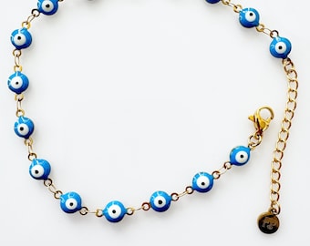 May include: Gold-toned anklet featuring blue and white evil eye beads. The chain is delicate, with a lobster clasp closure and an extender chain. The evil eye beads are evenly spaced along the chain.