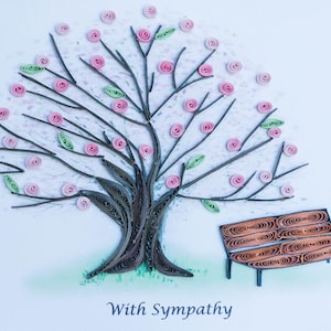 May include: A paper quilling art piece depicting a tree with pink flowers and green leaves. A brown bench sits beneath the tree. The text "With Sympathy" is written below the bench.