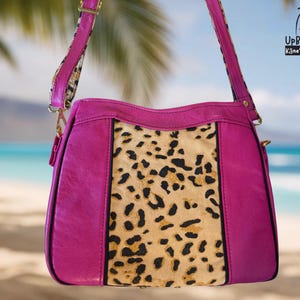 May include: A fuchsia-colored handbag with a leopard print center panel and a matching strap. The bag has gold-colored hardware and the text "UpBeat Bags Kāne'ohe, Hawai'i USA" is visible in the upper right corner.