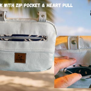 May include: White leather bag with a zip pocket and heart-shaped zipper pull. The bag has a patterned interior and a small logo patch. Text on the image reads "BACK WITH ZIP POCKET & HEART PULL" and "UpBeat Bags, Kaneohe, Hawaii USA."