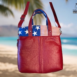May include: A red leather handbag featuring a top panel with a blue and white star pattern and red and white stripes. The bag includes two red leather handles, an adjustable shoulder strap, and the UpBeat Bags Kaneohe, Hawaii USA logo.