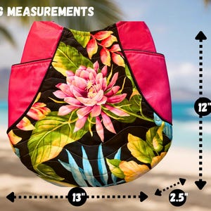 May include: A quilted tote bag with a floral design featuring a pink lotus flower and tropical leaves. The bag has a hot pink top and measures 12 inches high, 13 inches wide, and 2.5 inches deep.